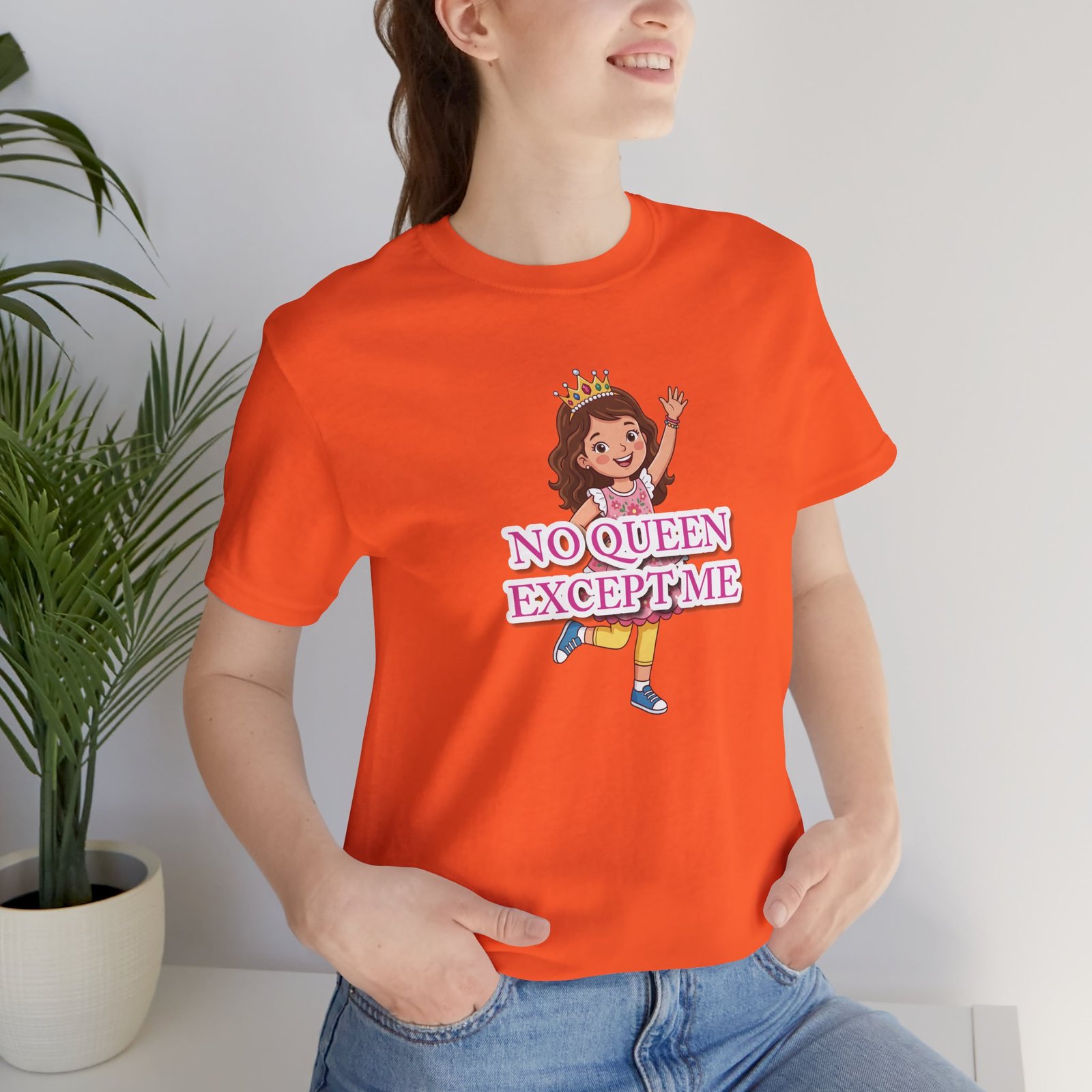 Girl wearing an orange t-shirt with a whimsical crown illustration and No Queen Except Me text.