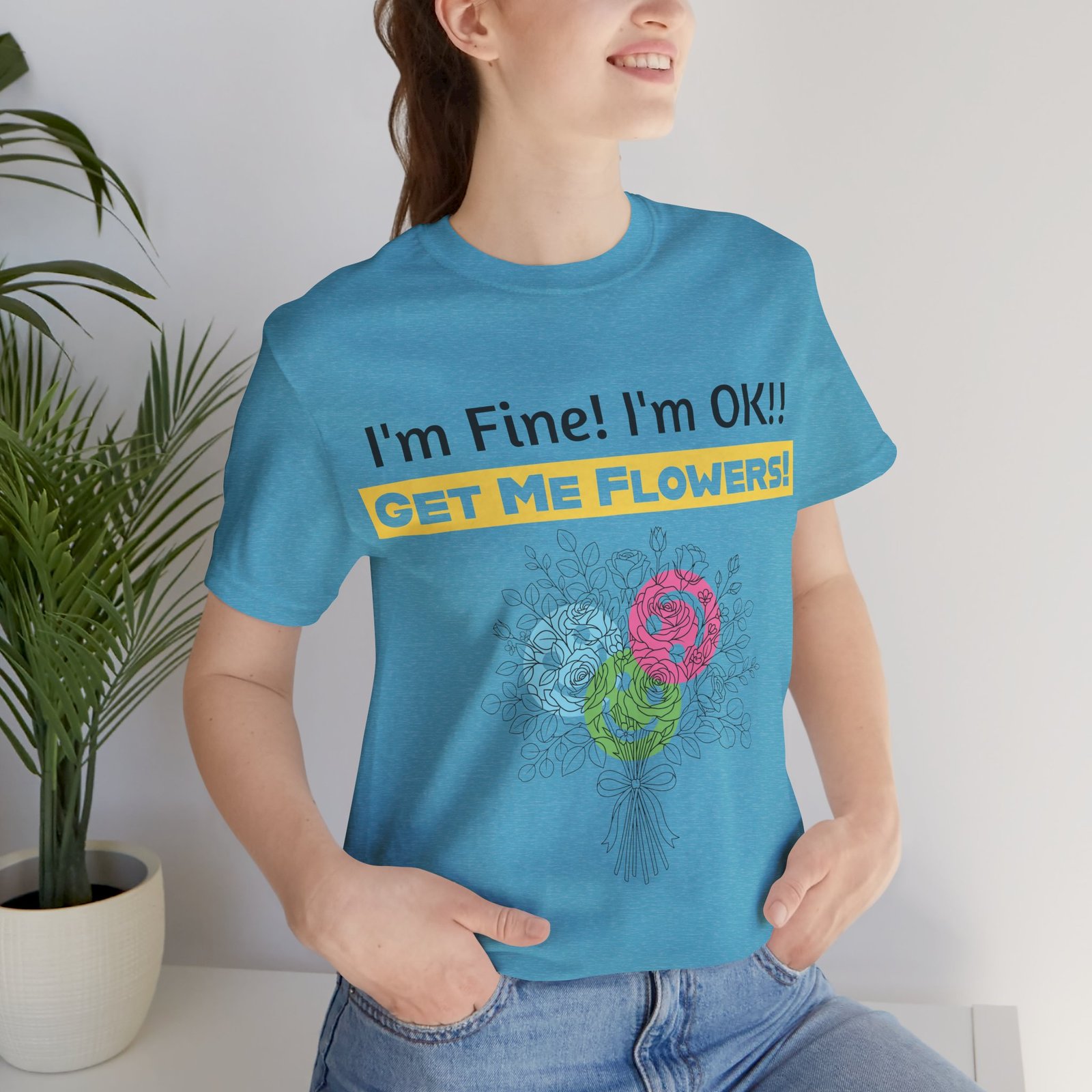 Light blue crew-neck tee with "I'm Fine! I'm OK!! GET ME FLOWERS!" text and a colorful abstract floral bouquet graphic.