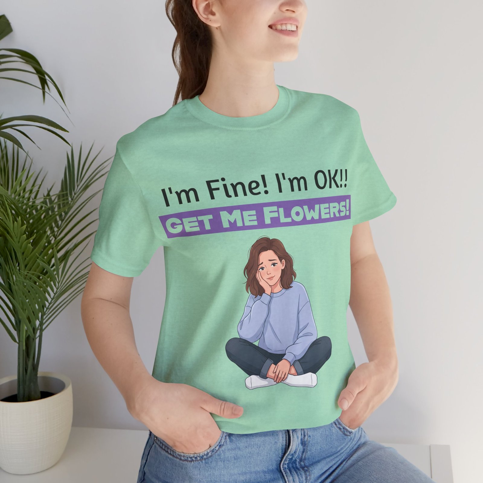Woman wearing a light green t-shirt featuring a cartoon girl and the funny text I'm Fine! I'm OK!! GET ME FLOWERS!