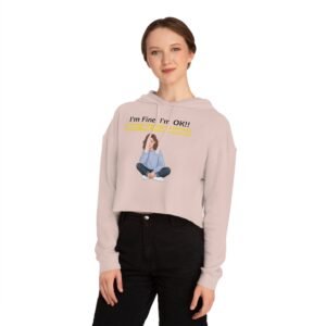 Woman wearing a light pink cropped hoodie with a graphic of a seated girl and yellow text saying "I'm Fine! I'm OK!! GET ME FLOWERS!"