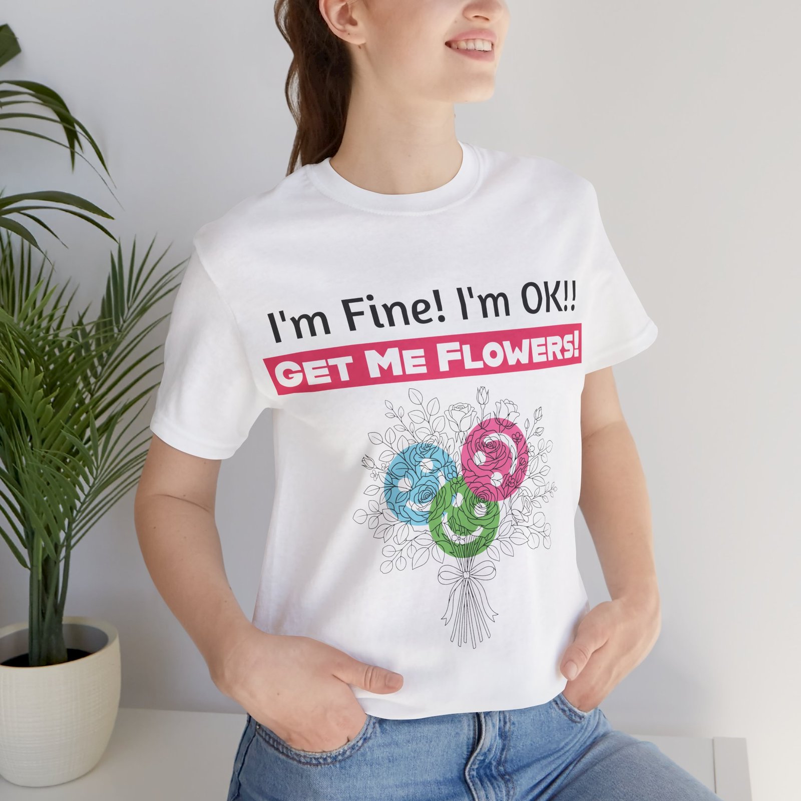 Woman wearing a white crew-neck T-shirt with funny "I'm Fine! I'm OK!! Get Me Flowers!" text and colorful floral graphic.