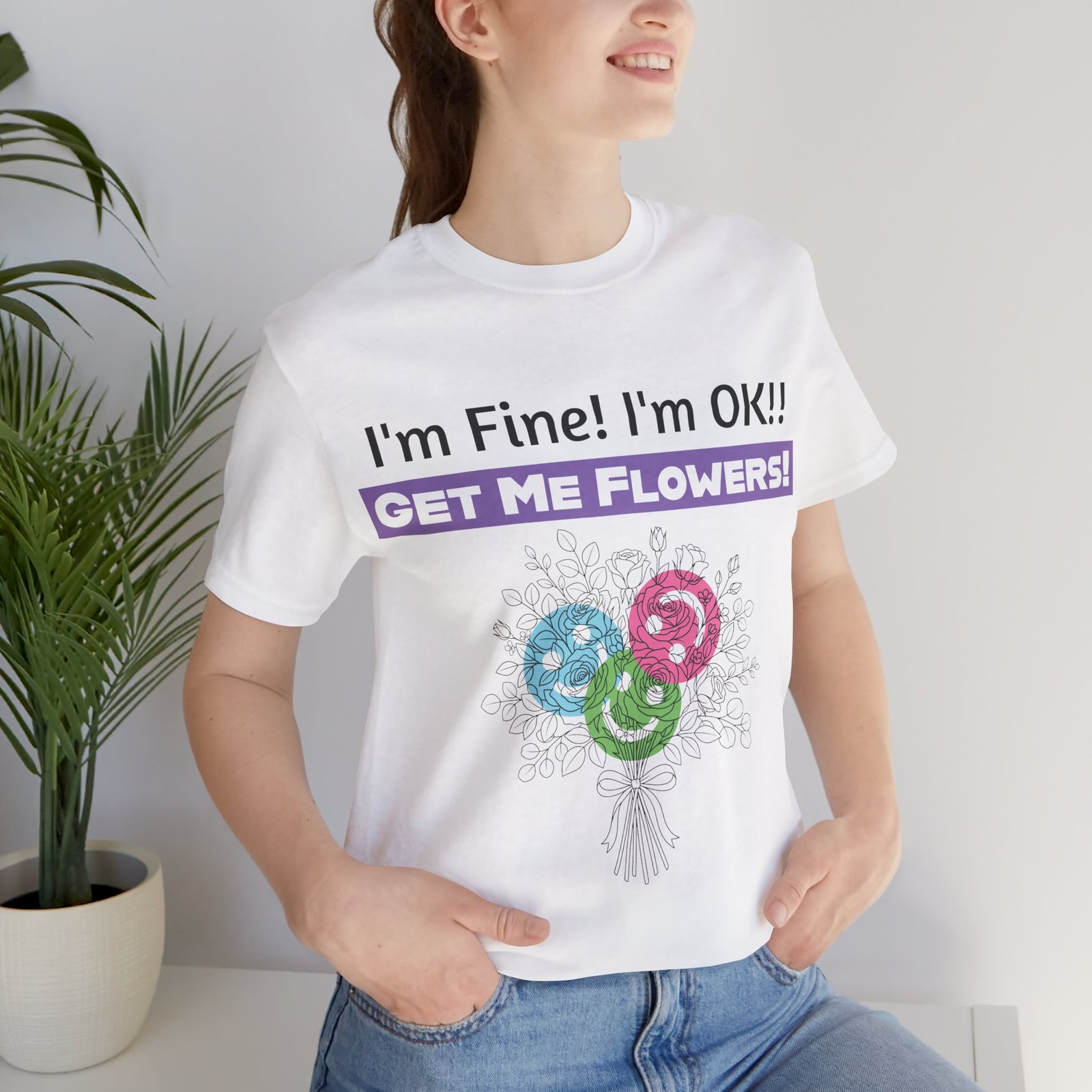 Woman wearing a white graphic t-shirt with the sarcastic text "I'm Fine! I'm OK!! GET ME FLOWERS!" and colorful flower art.